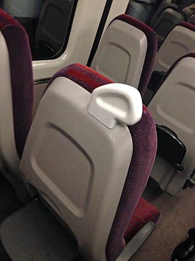 Close-up of train seats in dark red patterned fabric with a white plastic grab handle on the headrest