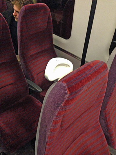 Train interior with maroon patterned seats; a glowing white headrest catches the light, a passenger seated behind