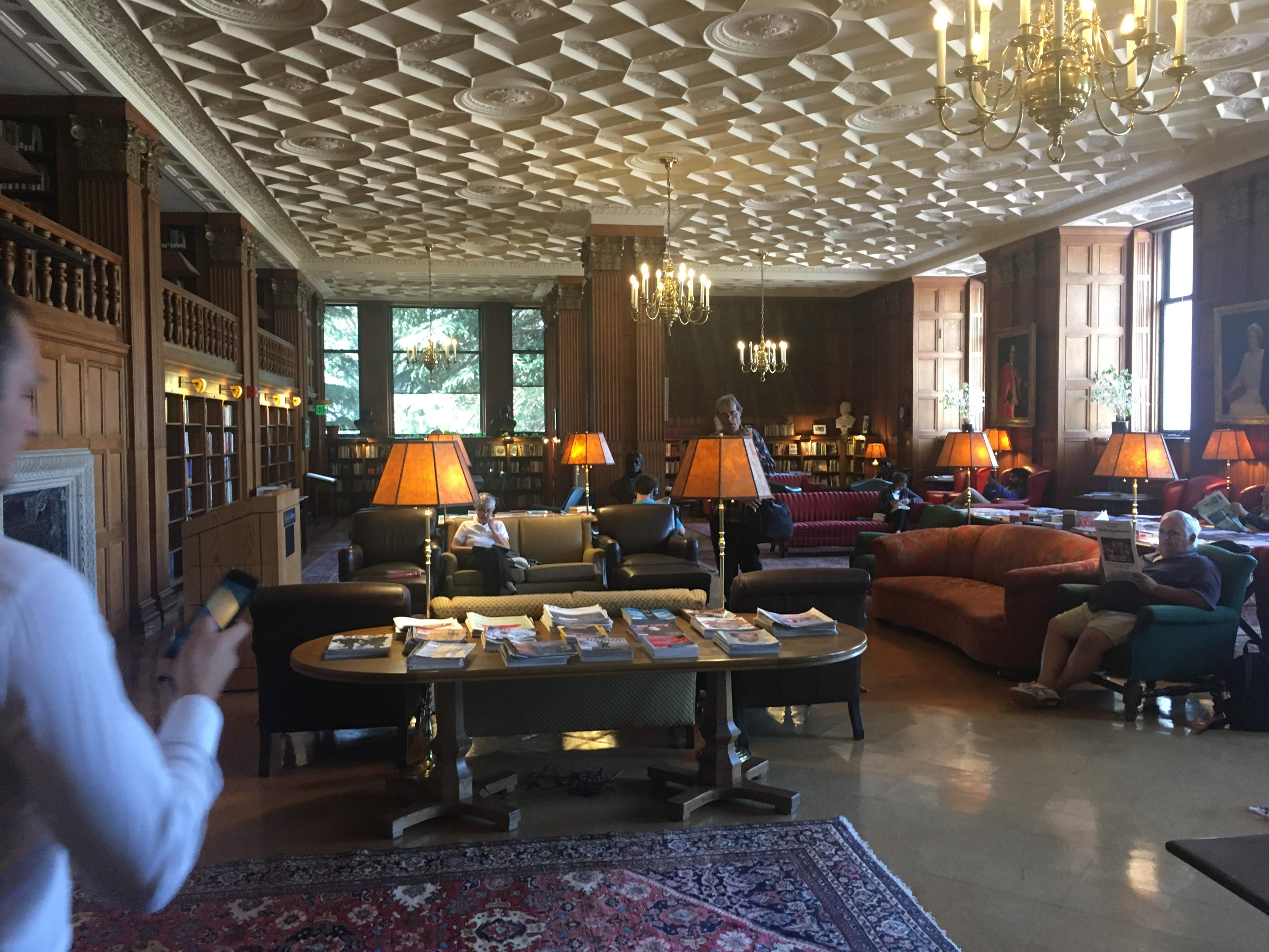 Grand wood-paneled library lounge with an ornate ceiling, chandeliers, sofas and reading tables.