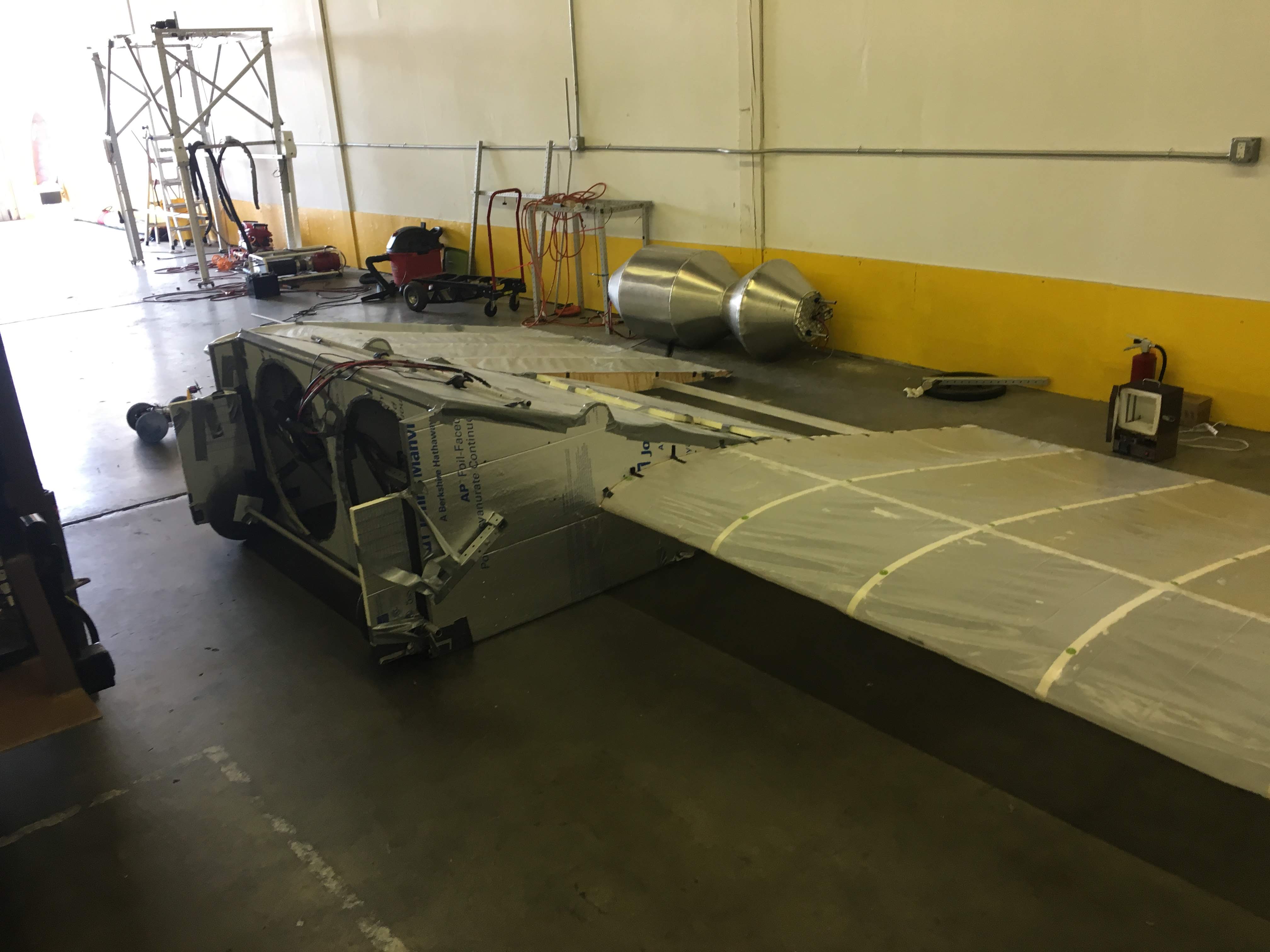 Large experimental aircraft wing and foil-clad fuselage under construction in a workshop.