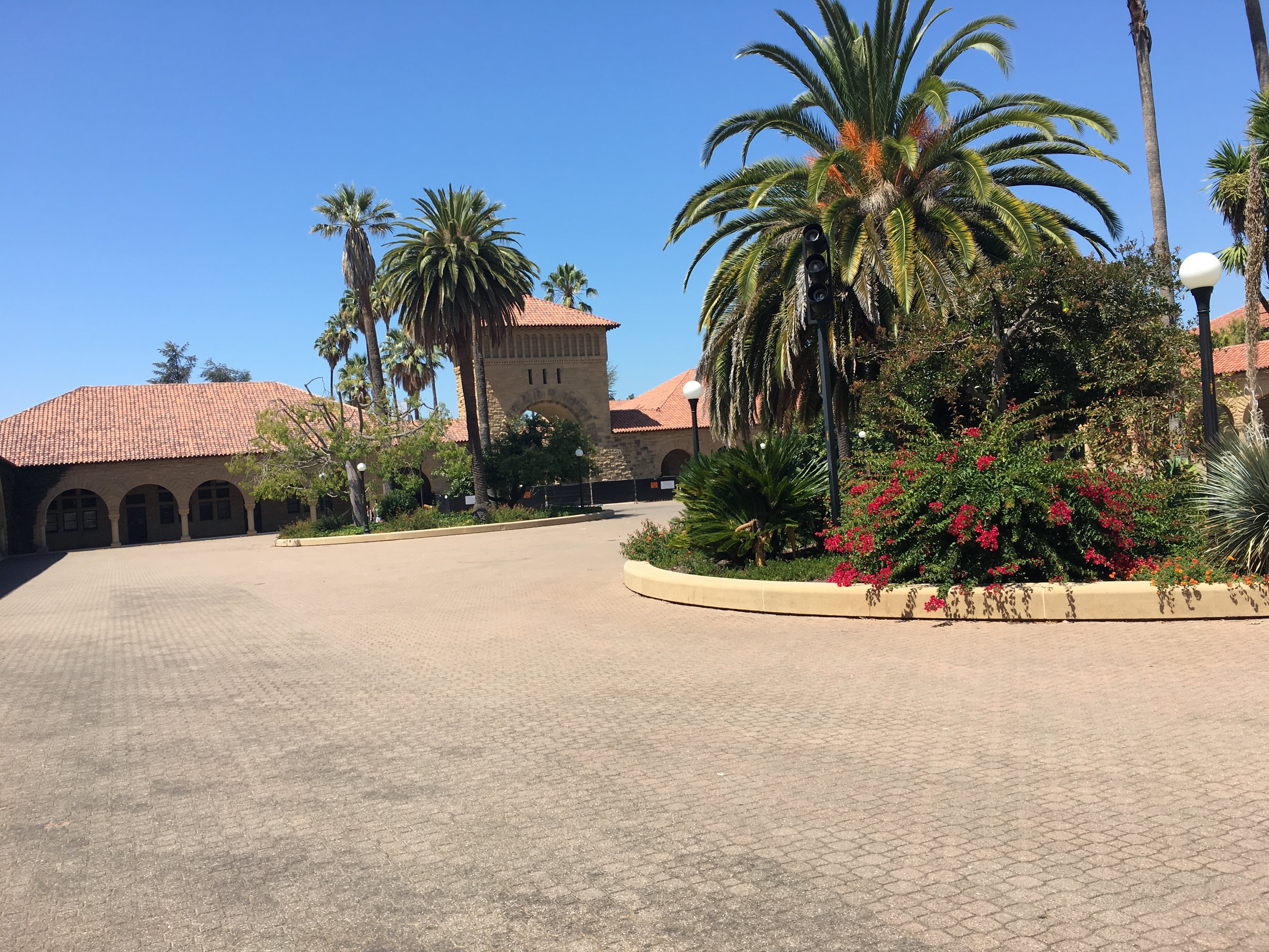 Stanford entrance plaza with an arched gateway, palm trees and a flowering planted island.