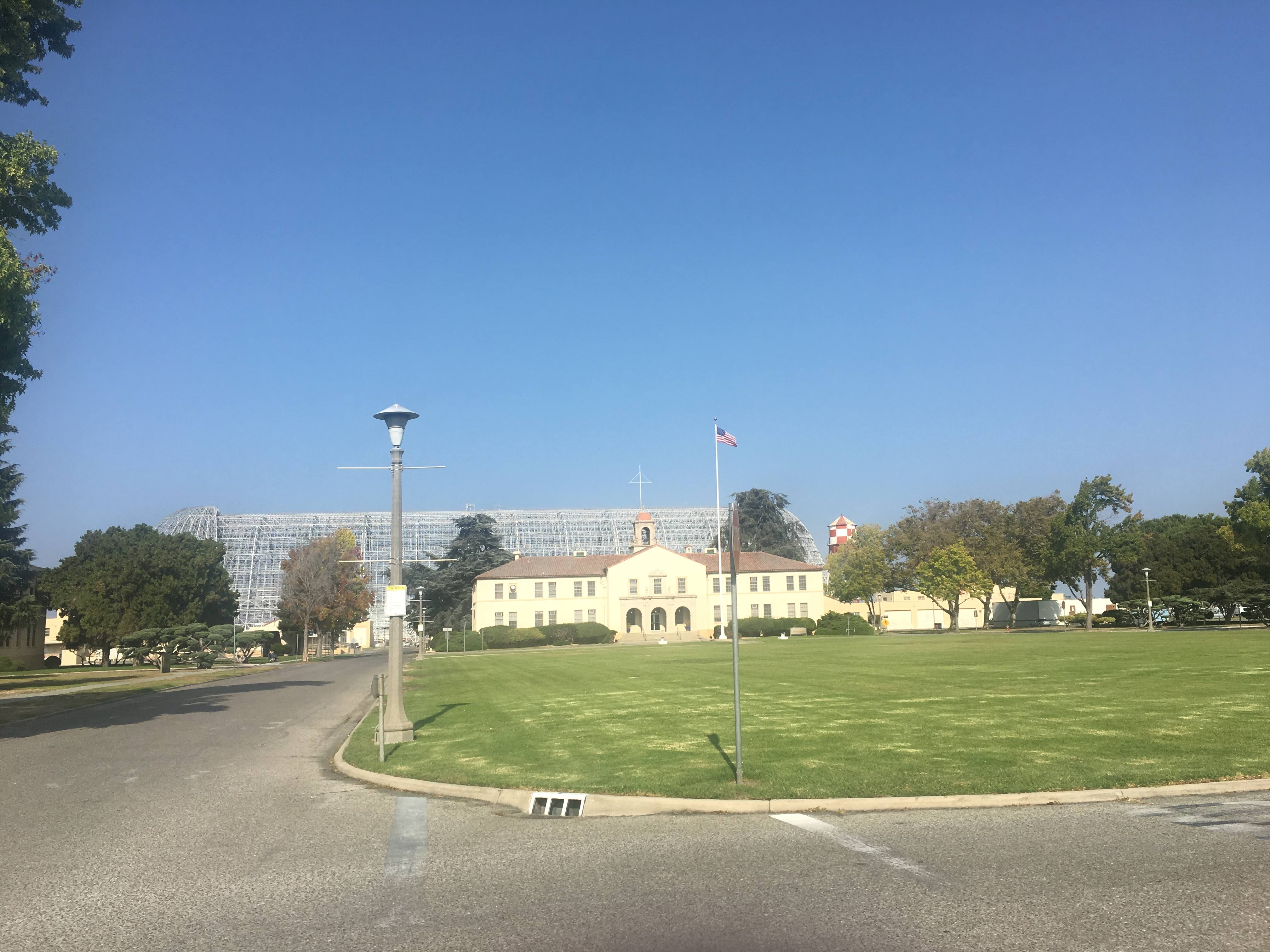 Historic base building and lawn with the vast NASA Ames hangar framework rising behind it.