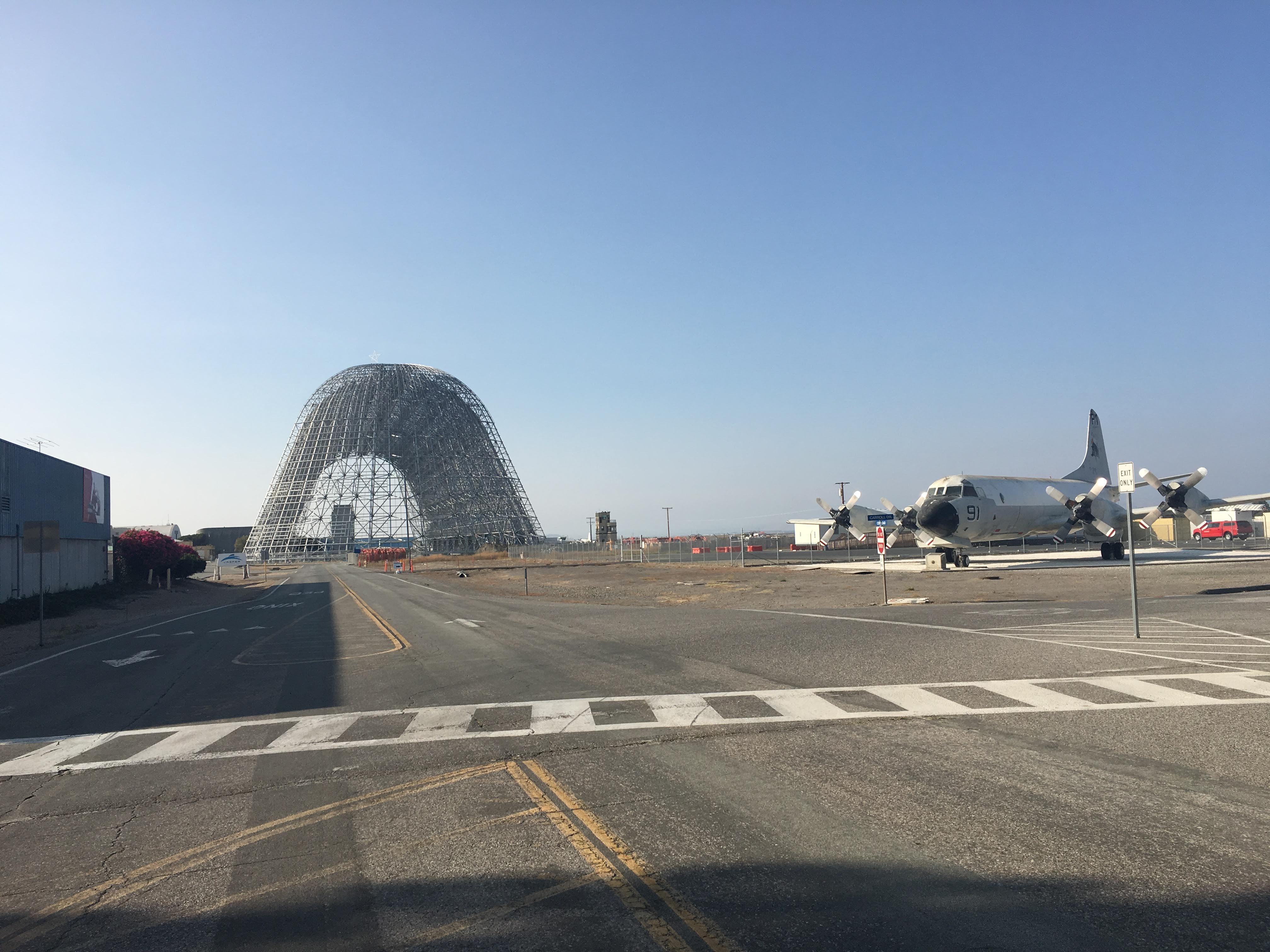 The domed steel skeleton of NASA Ames Hangar One with a parked navy turboprop plane nearby.