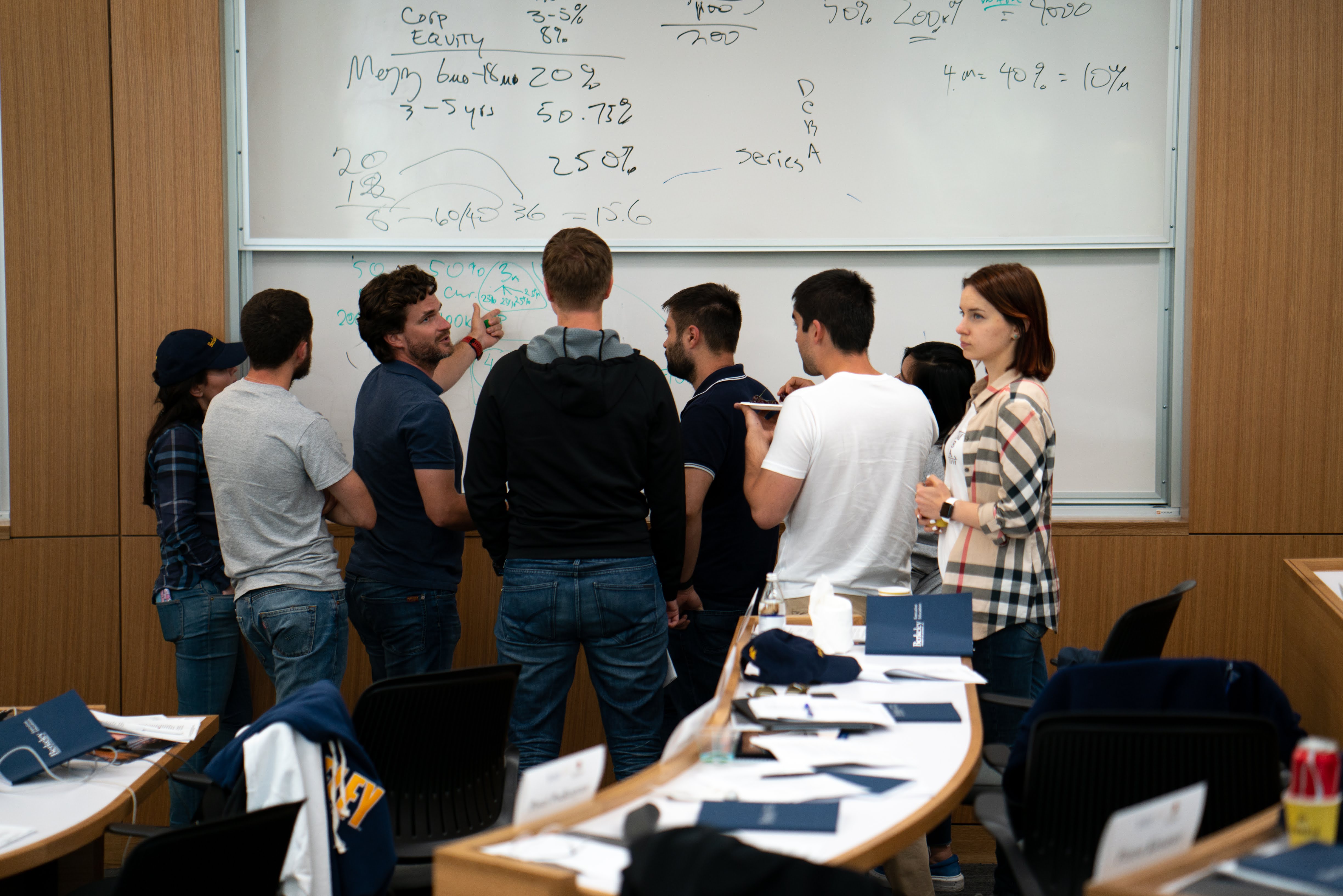 Group of people standing at a whiteboard covered in finance figures during a workshop.
