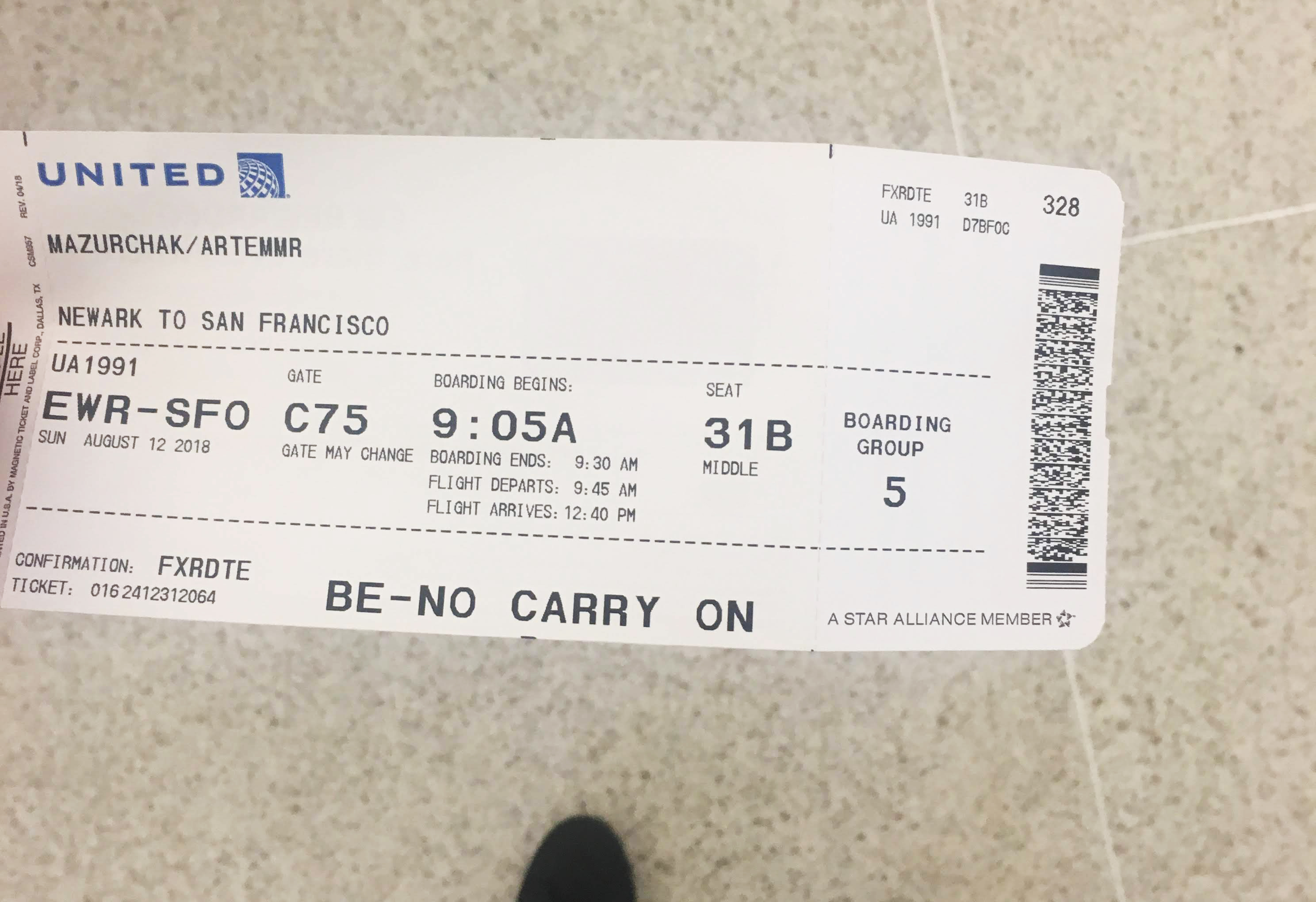 United Airlines boarding pass, Newark to San Francisco, flight UA1991, seat 31B, held over a tiled floor.