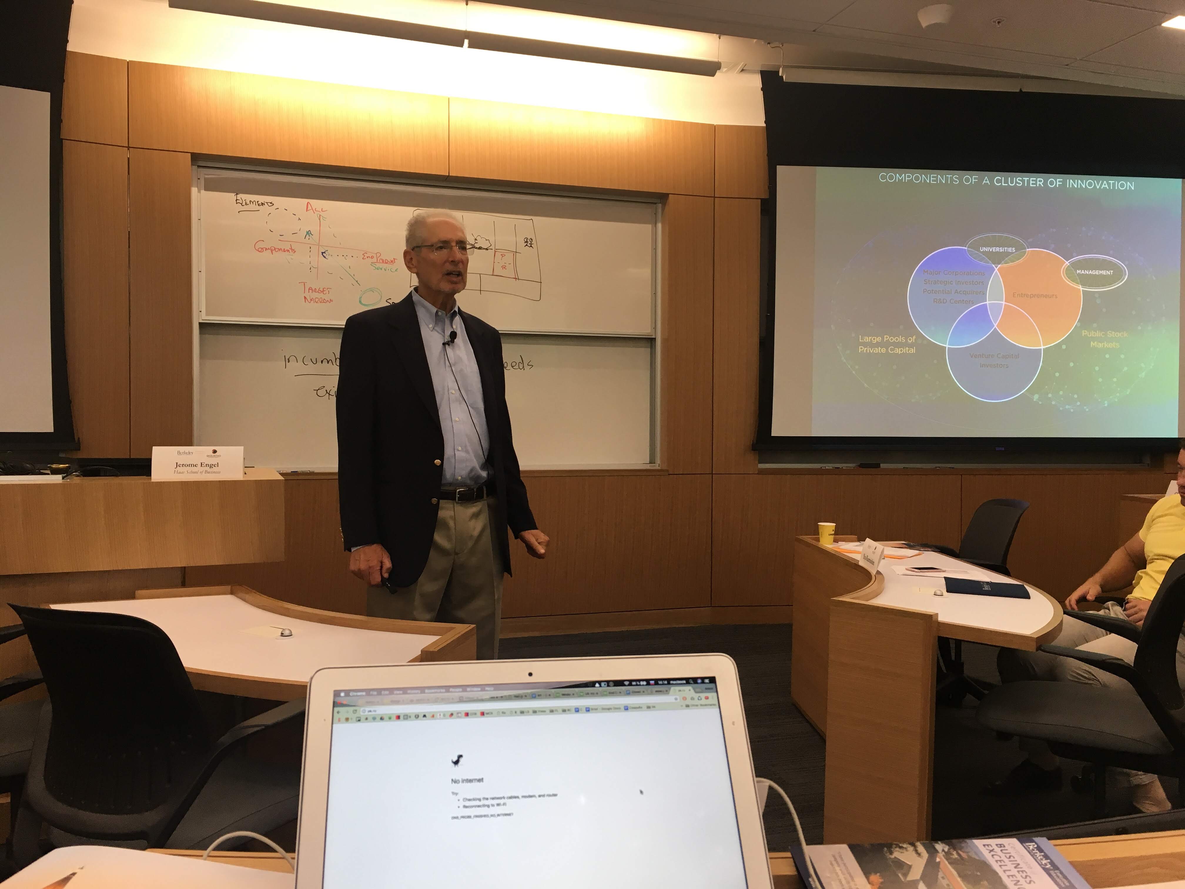 Speaker presents beside a Components of a Cluster of Innovation slide in a Berkeley classroom.