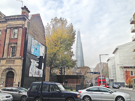 London street with The Shard rising in the distance, a mural on a wall and cars in the foreground