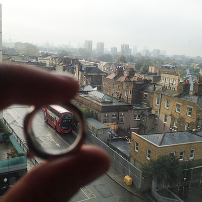 A hand holds a round lens showing an inverted view of a London street with a red bus