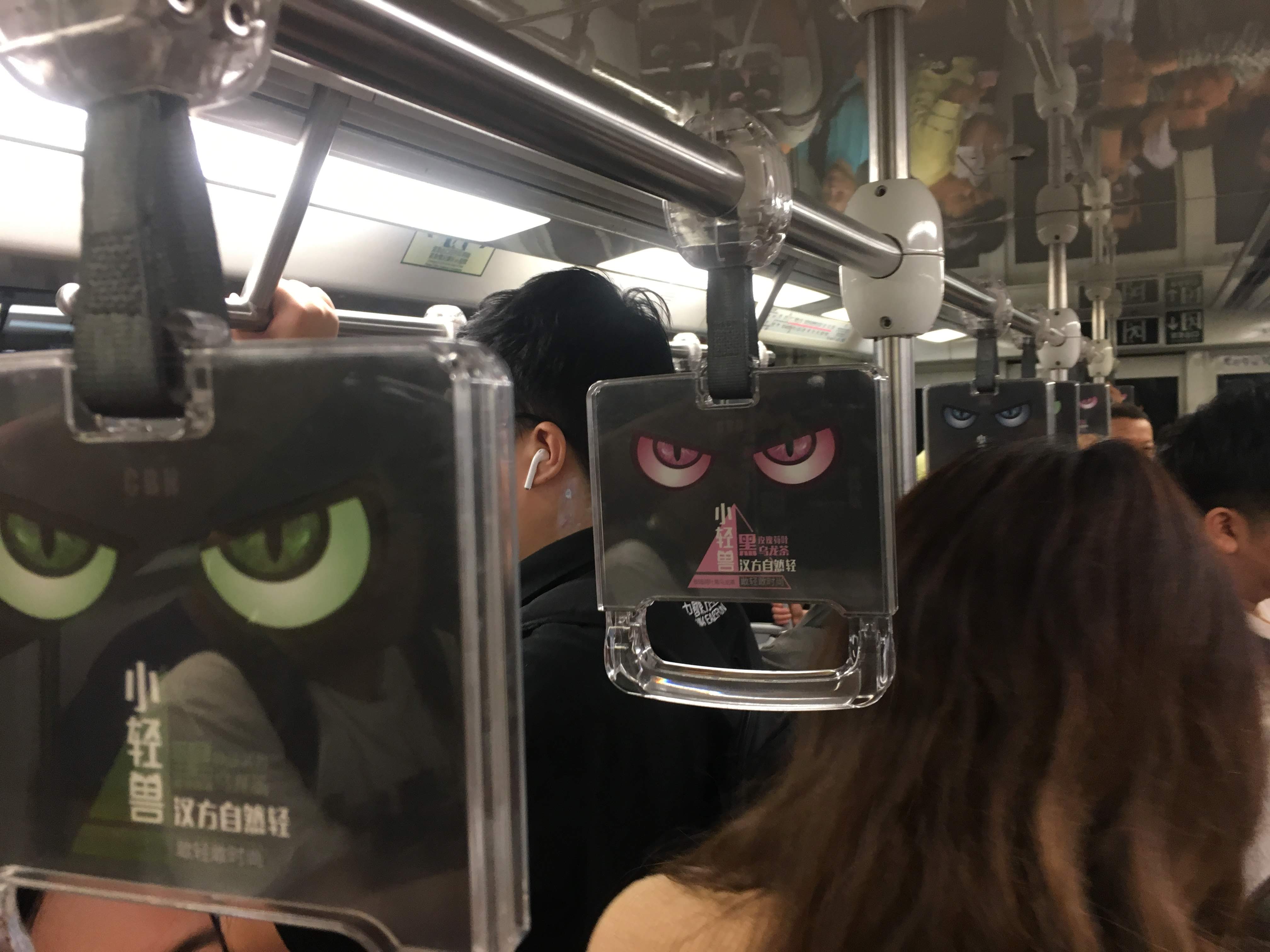 Crowded subway car with transparent hand grips printed with cartoon animal eyes as advertising.