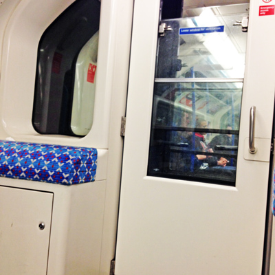 Tube carriage door and a seat upholstered in blue patterned fabric, passengers visible through the glass