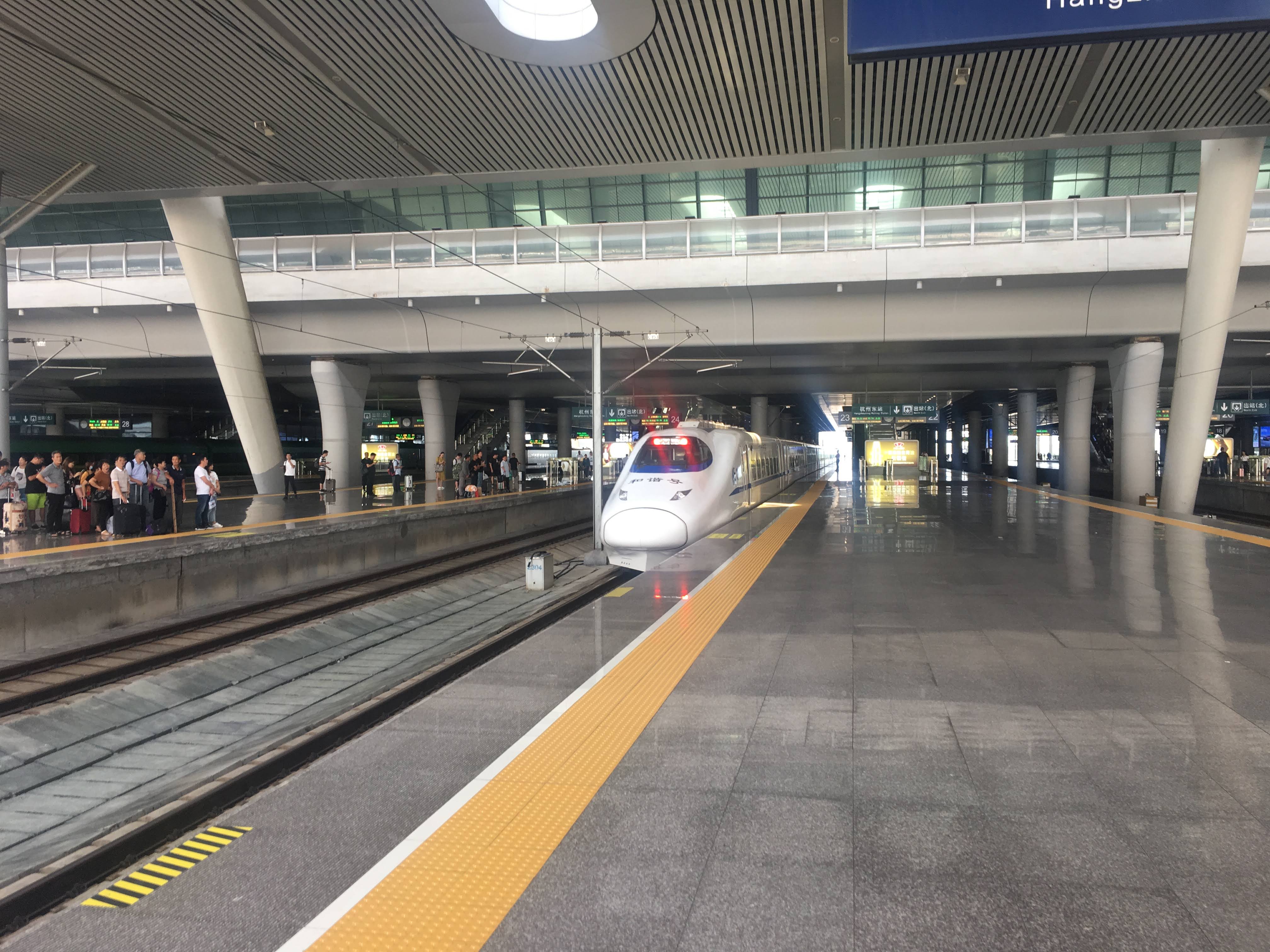 White high-speed train arriving at a station platform as passengers wait with luggage.